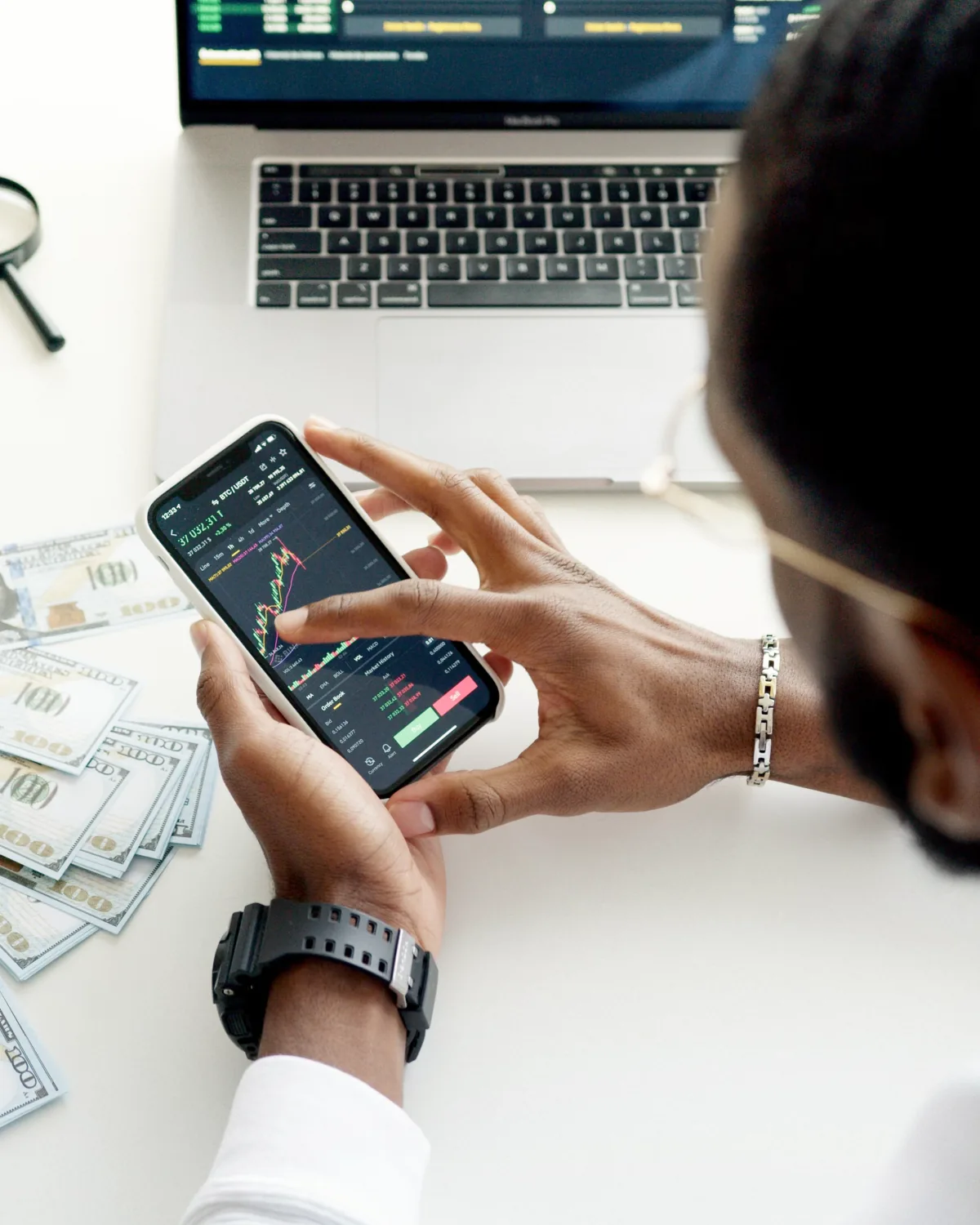 Investor reviewing a market chart on a smartphone beside a laptop